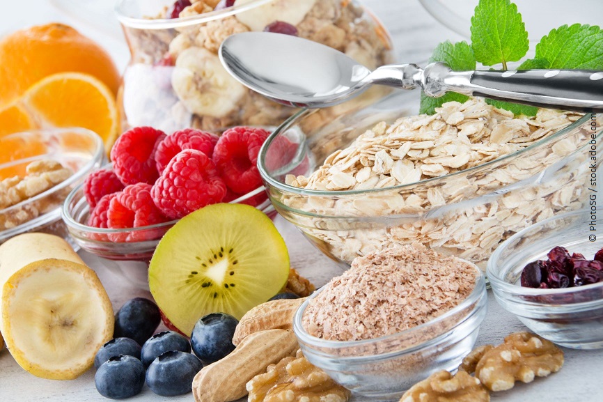 Verschiedenes Obst, Nüsse und Haferflocken liegen verteilt auf einem Tisch. 